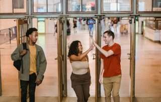 Three students exiting a building while 2 of them are high-fiving each other